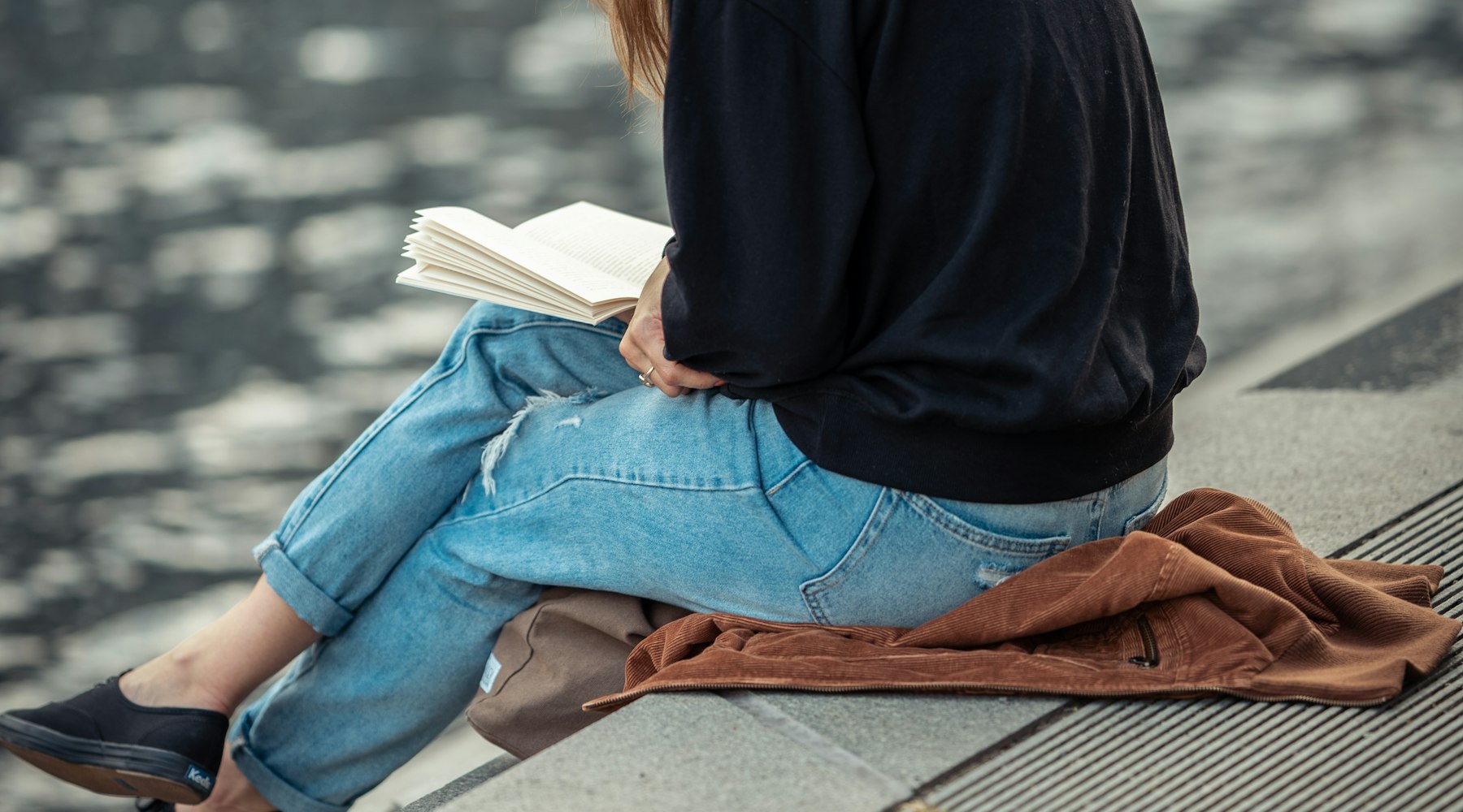 Someone sitting on a quay by the water, reading