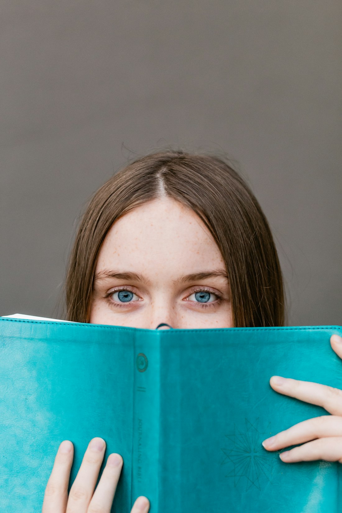 Someone looking at you over the top of a teal book held up to their face